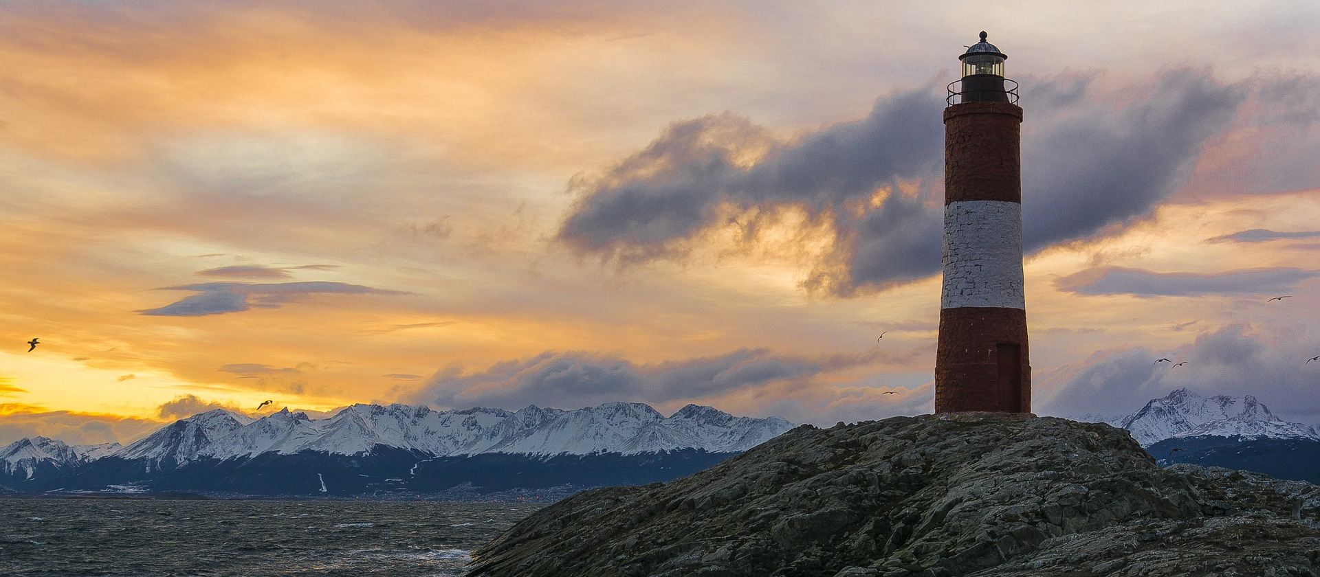 Lighthouse overlooks sea and mountains in Ushuaia, Argentina.