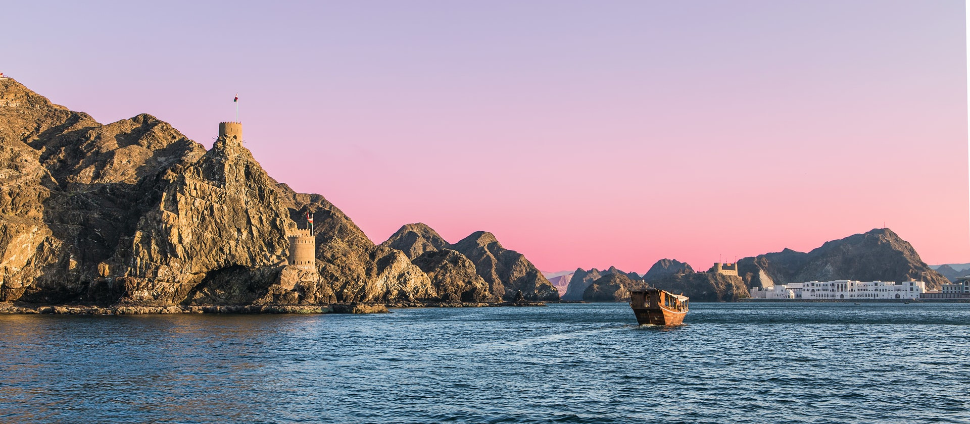 Traditional boat on the sea near cliffs with pink sunset, Oman