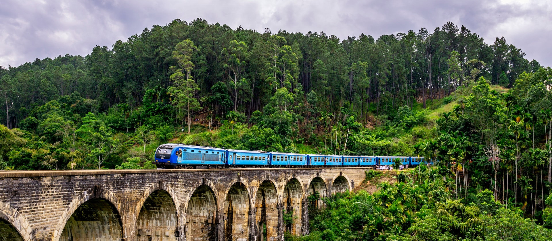 Blue train surrounded by trees crosses Nine Arches Bridge, Ella, Sri Lanka