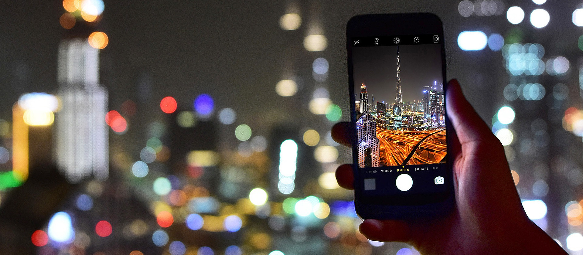 A woman taking a photo of the Burj Khalifa in Dubai on a phone.